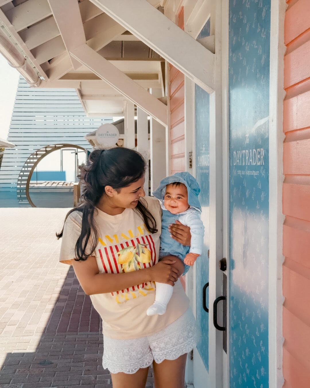 Arya smiling in her amma's arms by a coral beach storefront