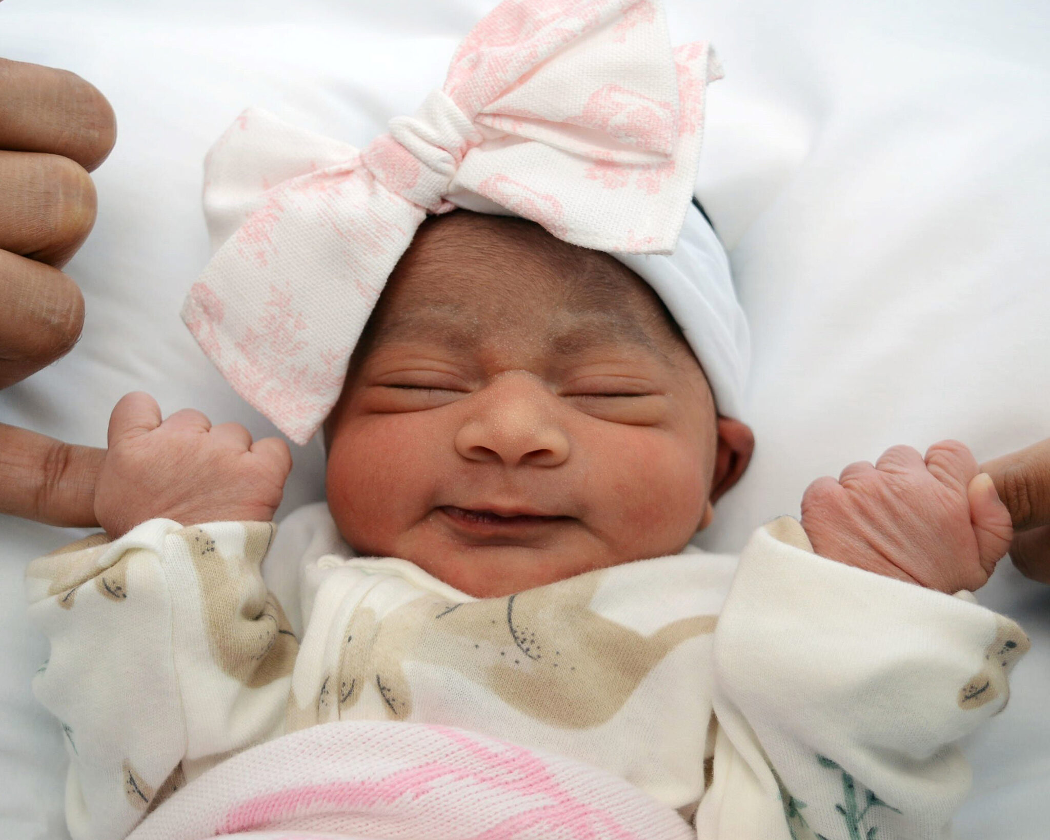 Newborn Arya smiling in a big pink bow, holding two fingers